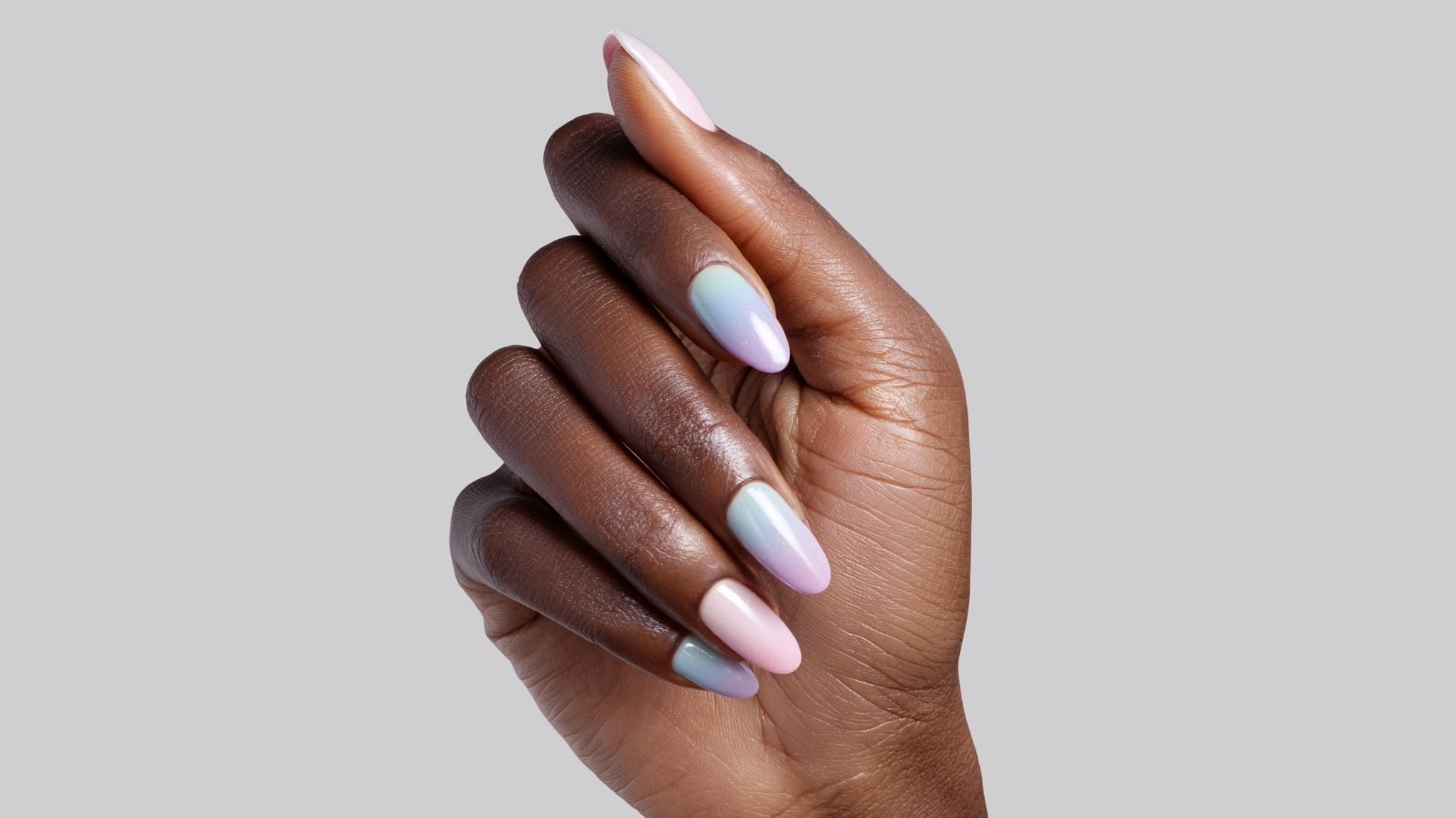 Close-up of a hand with long pastel-colored acrylic nails in a gradient design against a neutral background