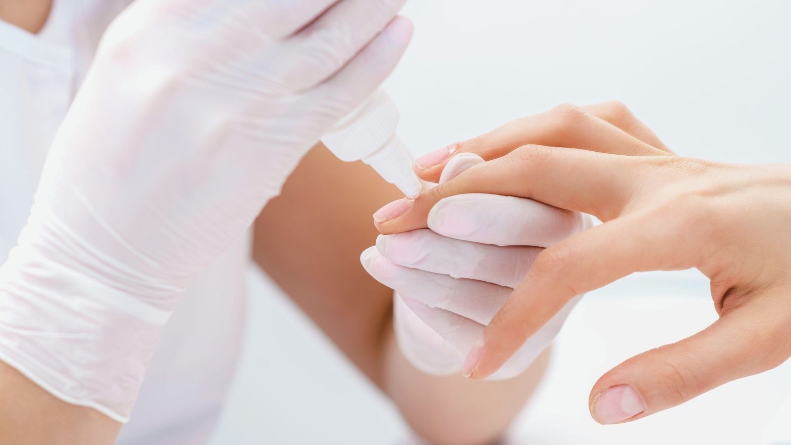 Close-up of a nail technician applying nail glue to a client’s fingernail during manicure