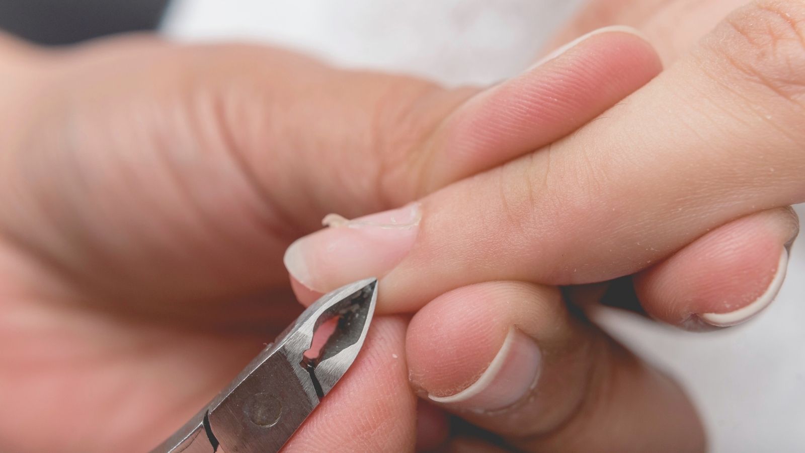 Close-up of a person trimming a hangnail with a cuticle nipper during nail care